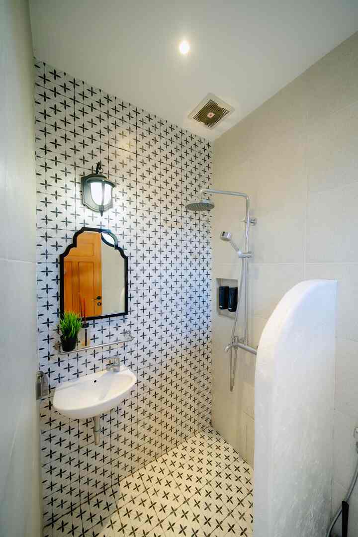 Mediterranean bathroom with white and black patterned tiles, featuring a washbasin and shower fixtures in a clean layout