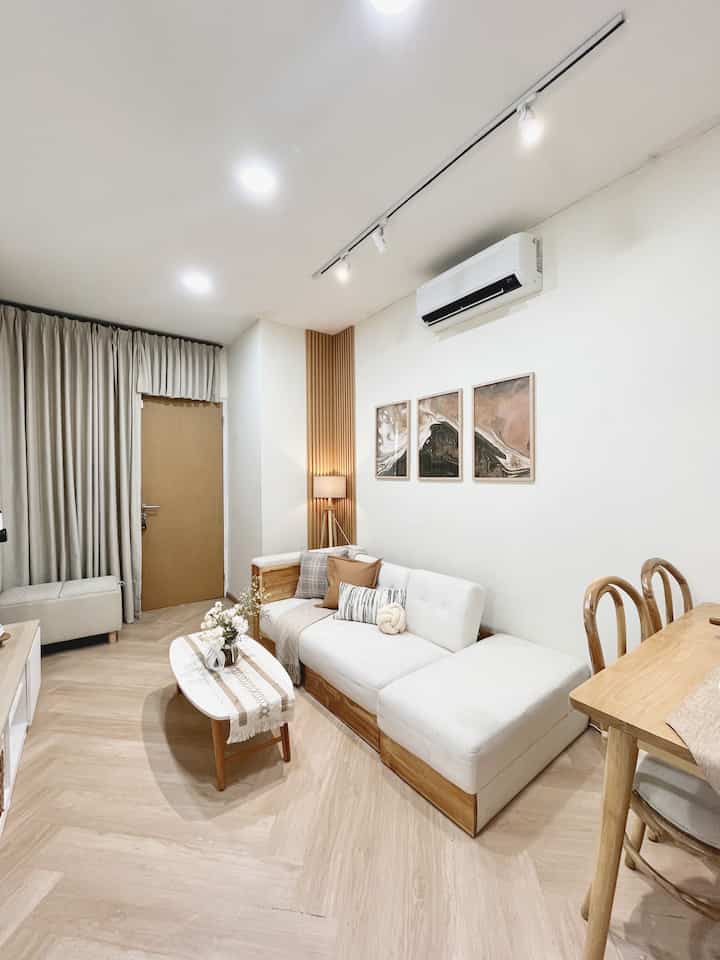 Bright living room with white and natural wood tones featuring modern sofa and wooden dining table creating a clean atmosphere