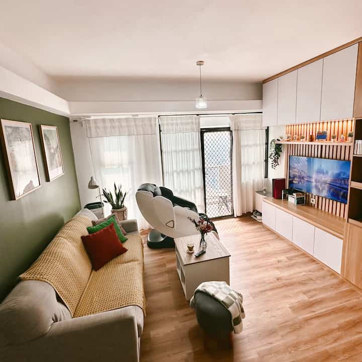 Natural tone living room with green accent wall, featuring sofa, armchair, and TV stand in a clean cozy setting