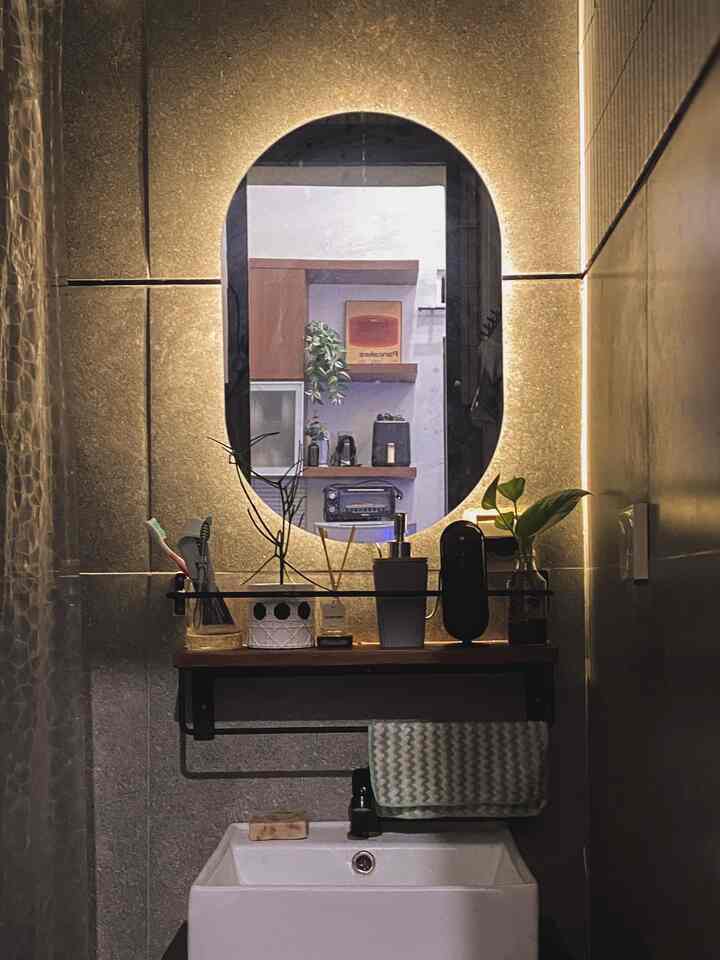 Warmly lit bathroom with oval LED mirror, sink, towel, and plants arranged in a cozy setting