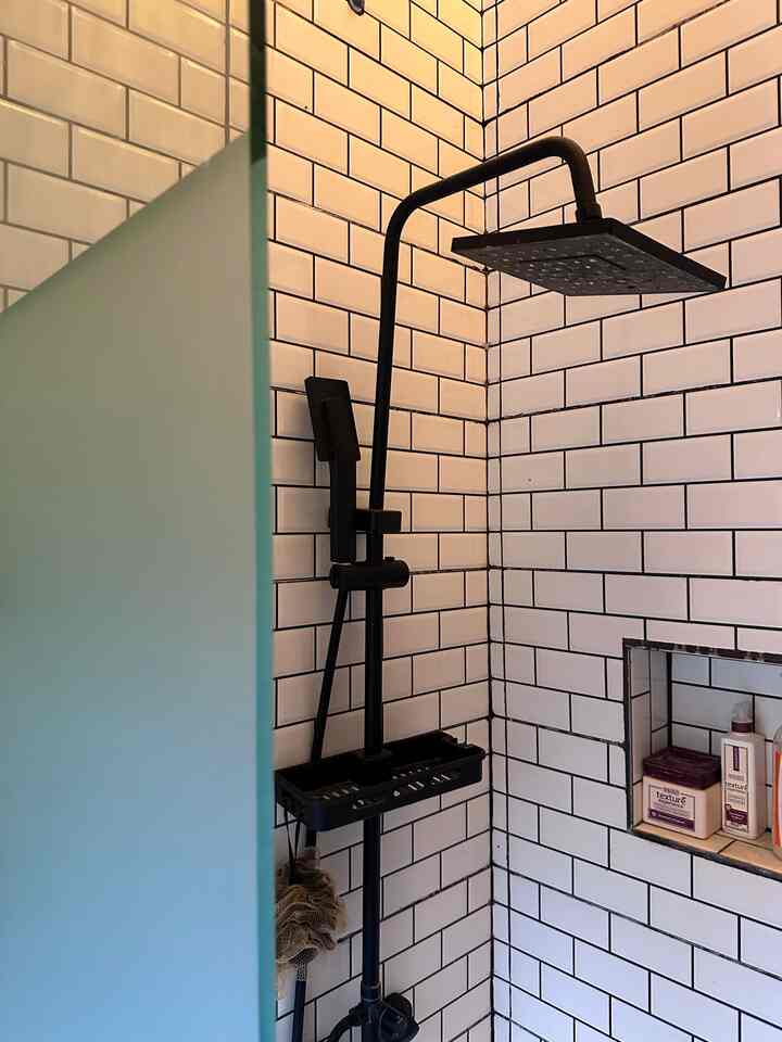 Bathroom space featuring white tiled walls and black shower fixtures