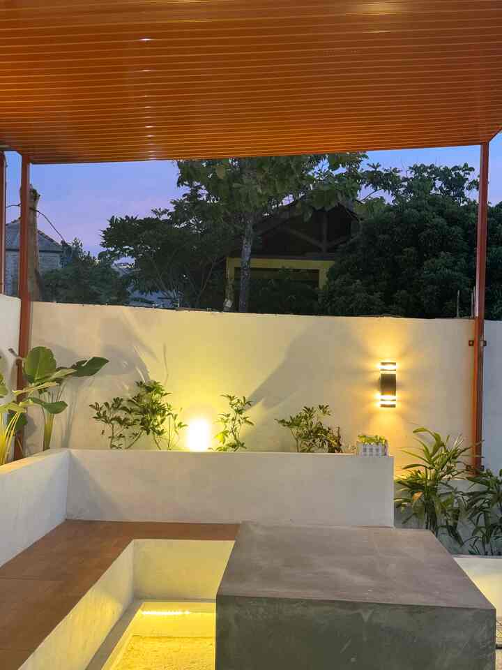 White-walled balcony space with plants, warm wall sconces, and modern outdoor seating creating a cozy atmosphere