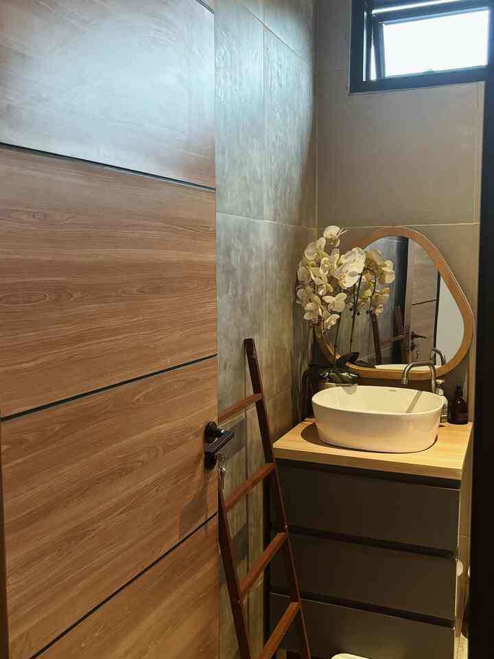 Industrial bathroom with gray tiled walls, wood-tone door, dark gray cabinet, white vessel sink, and orchid decor