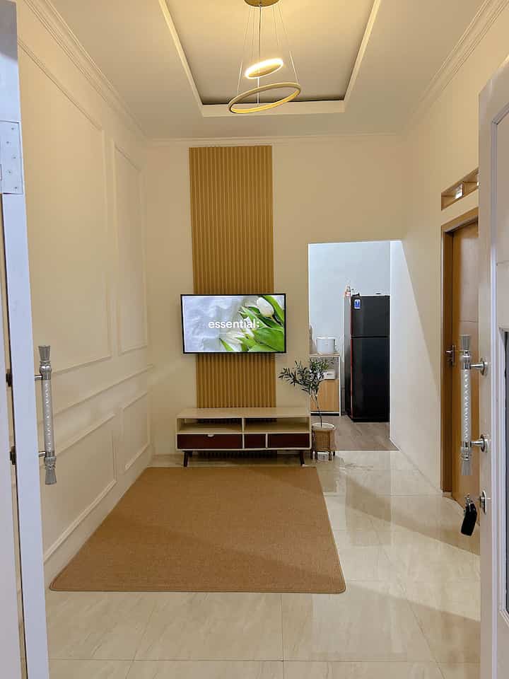 Narrow minimal living room in white and brown tones, featuring a central TV and carpet with a clean, uncluttered look