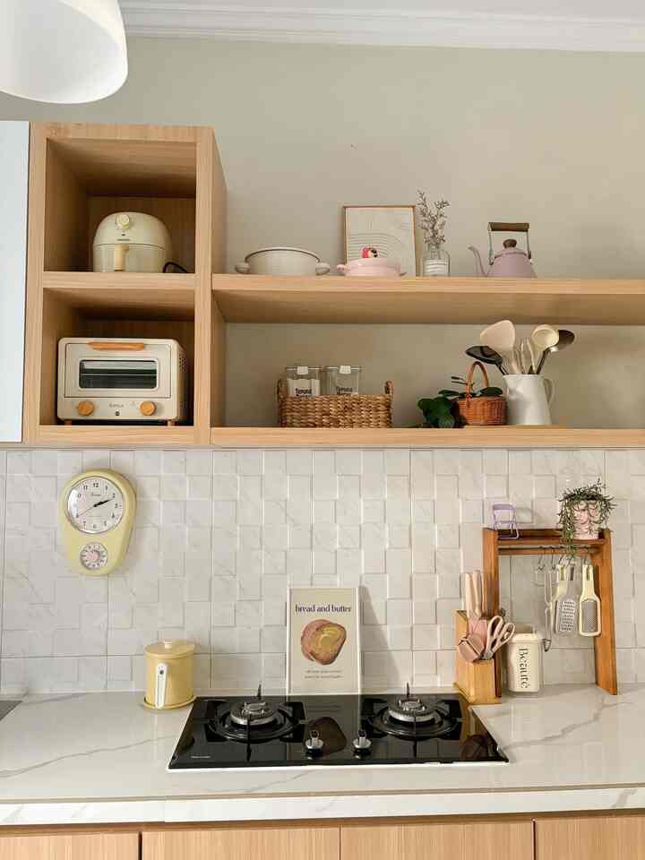 Cozy kitchen with white tiled walls and wood tone cabinetry, featuring kitchen utensils and a wall clock