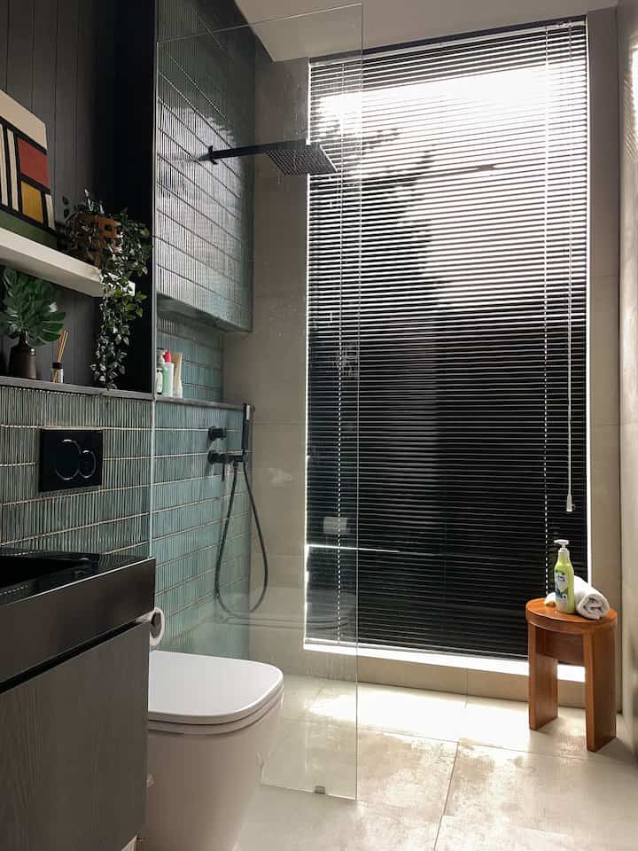 A black and gray toned bathroom featuring blinds, shower booth, and a wooden stool, presenting a modern bathroom interior