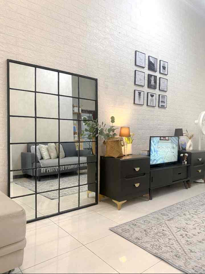 A Nordic-style living room with white walls and black furniture, featuring a large grid mirror and gray sofa in a clean setting