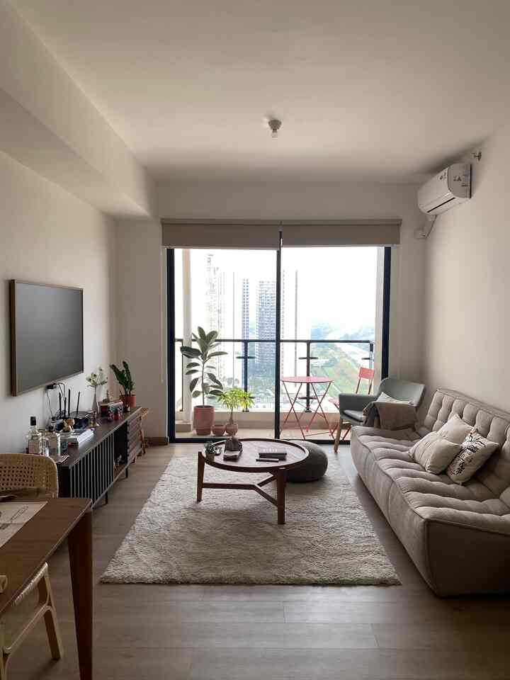 Natural tone living room with SPC flooring, beige sofa, armchair, round coffee table, carpet, and plants creating a cozy atmosphere