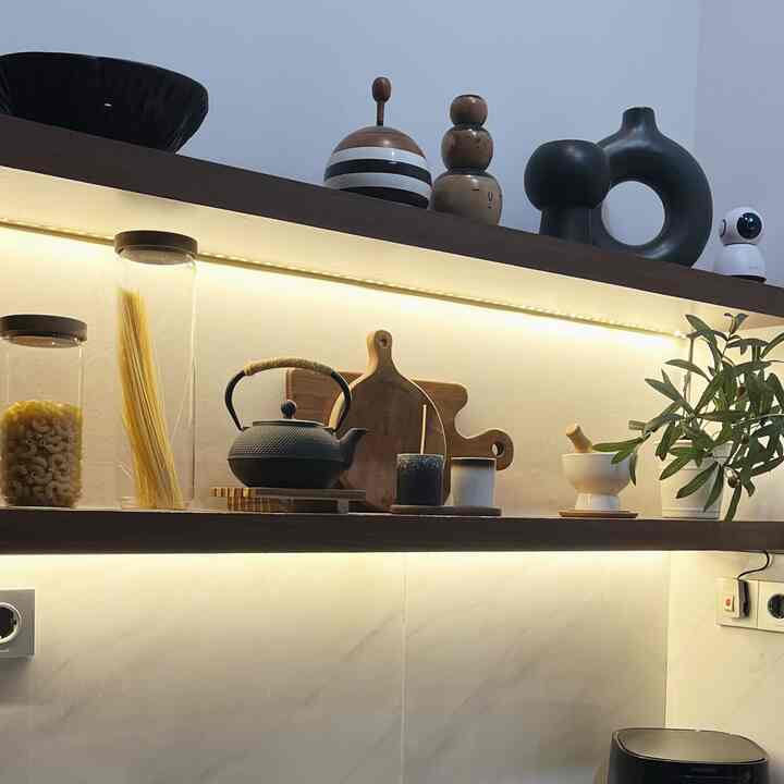 Warm-lit kitchen featuring wood tone shelves with organized kitchen utensils and storage jars, creating a cozy atmosphere