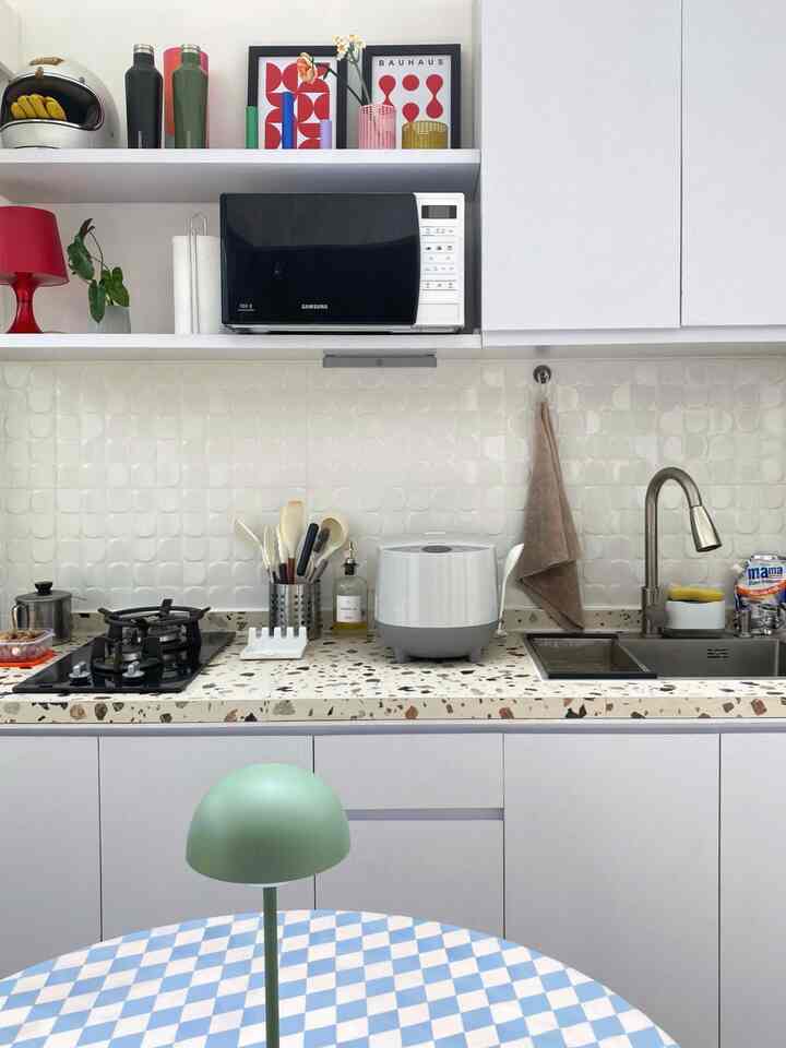 Small kitchen with dominant white and natural tones, featuring colorful accessories and a green table lamp creating a cozy atmosphere