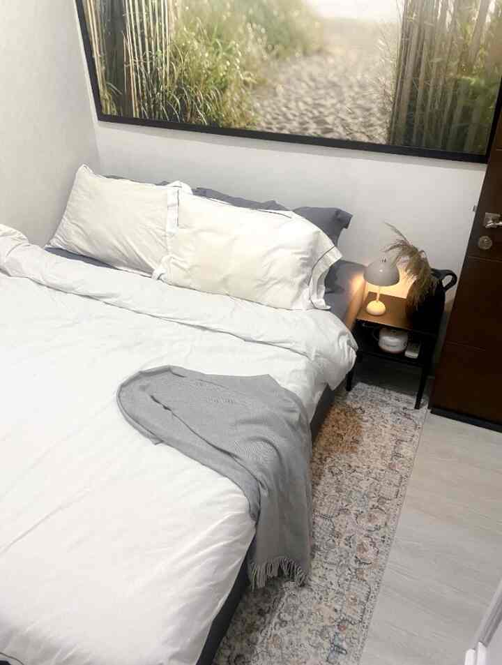 White and gray toned bedroom featuring bed, bohemian rug, table lamp, and natural decor creating a cozy atmosphere