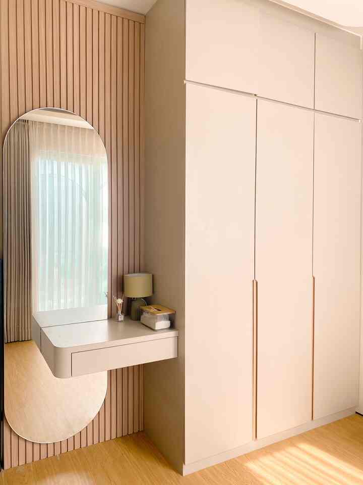 Bright beige and wood tone bedroom featuring a large closet, vertical mirror, and a table lamp with a minimalist modern vibe