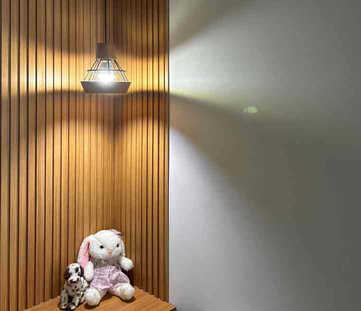 Cozy bedroom corner with warm wood tone wall paneling and pendant light, featuring children's plush bunny and dog toys