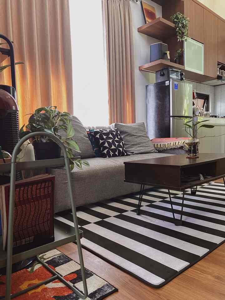 Gray sofa and brown coffee table in a compact, tidy living room with gray curtains and a black-and-white striped carpet creating a balanced interior
