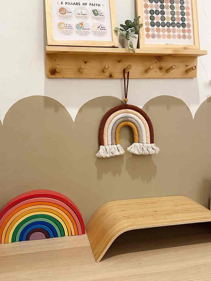 Beige wall and wood tone furniture create a cozy kids' room featuring wooden rainbow toy blocks and macrame decor