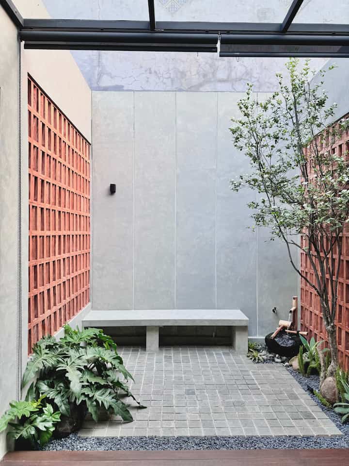 Natural tone small entrance sideyard featuring concrete bench, bamboo fountain, and green plants creating a cozy atmosphere