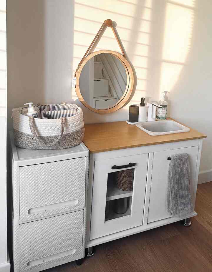 Clean bathroom space featuring a white cabinet with wood tone countertop, round mirror, and assorted dispensers on top