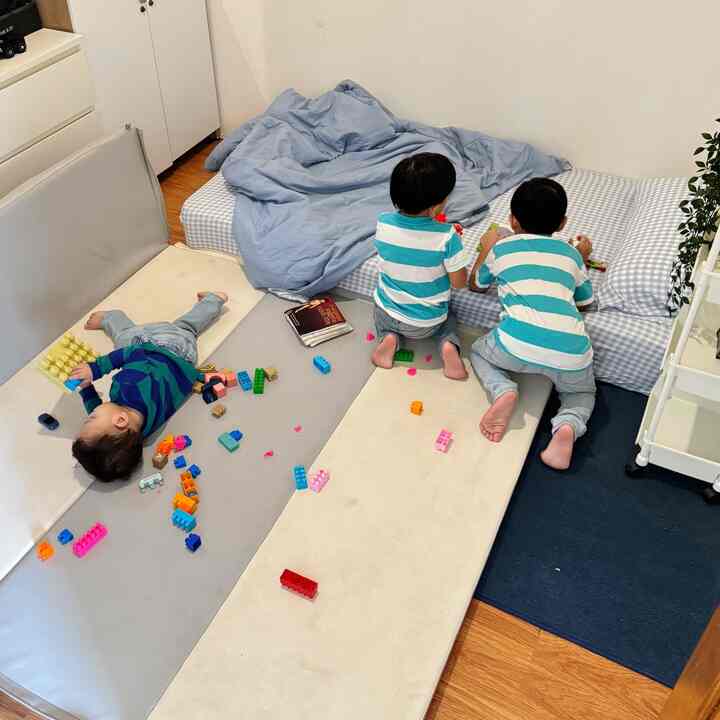 Natural-colored kids' room featuring three children playing with toys on checkered mattress and large floor play mats
