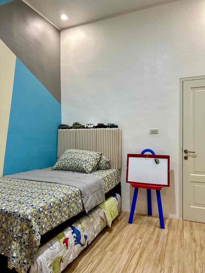 A kids' room with white walls featuring a blue triangular accent, striped bed, and a child’s whiteboard creating a cozy atmosphere