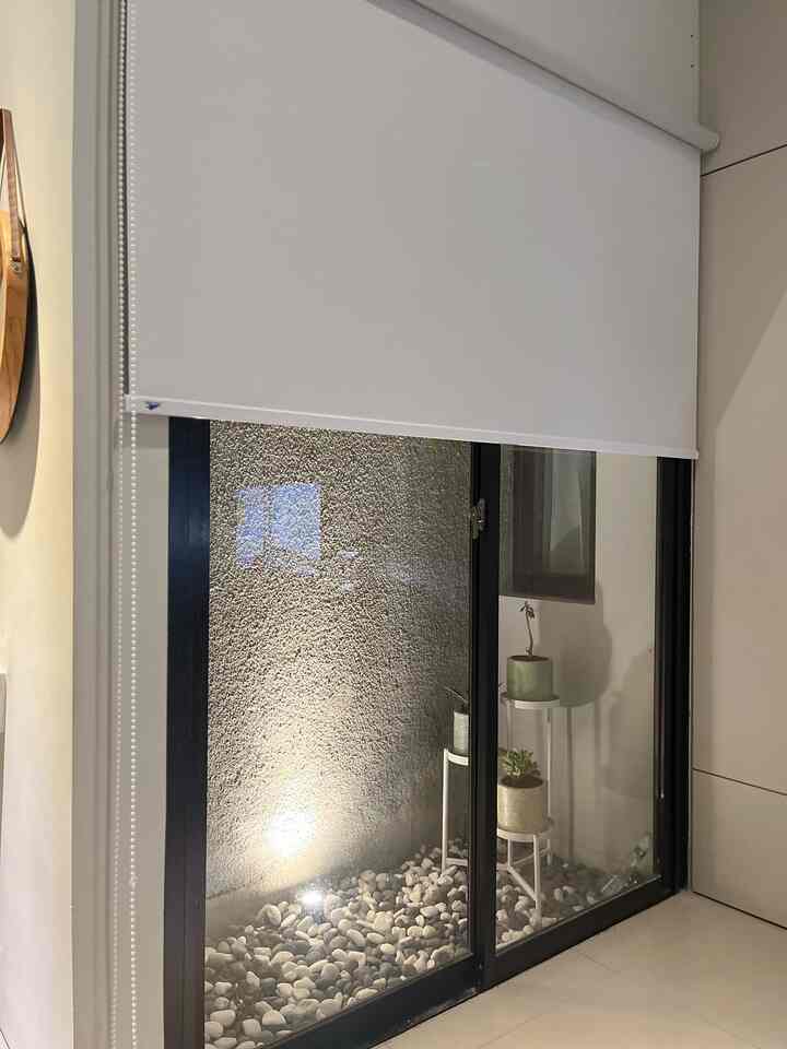 Narrow balcony-like space with white roller blinds, black and white gravel, natural modern vibe highlighted by white plant stands and terracotta pots.
