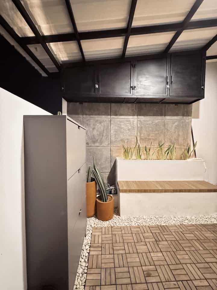 Modern entrance area with gray shoe cabinet and wood tone decking floor, featuring natural color tones and plants in a functional storage space