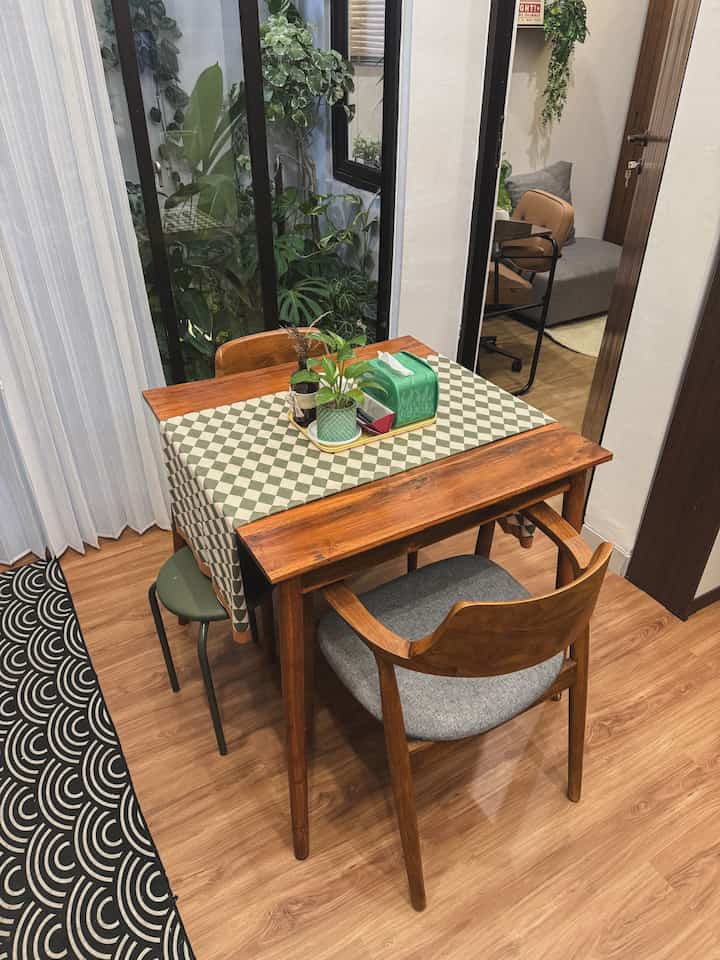 Natural wood tone compact dining room with three wooden dining chairs and table, complemented by green plants and minimal decor