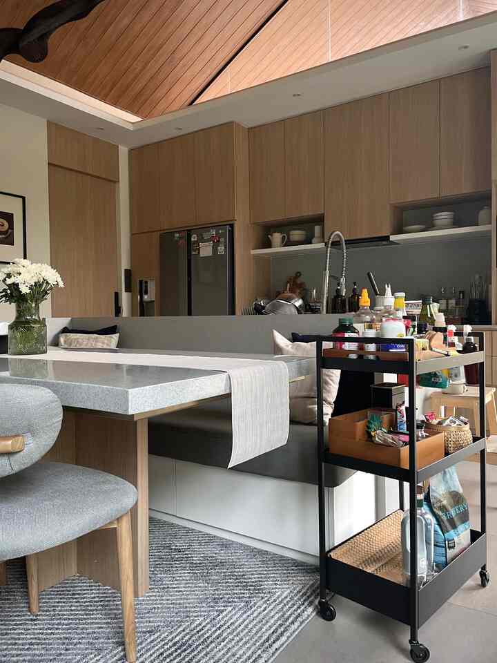 Wood tone kitchen space featuring a black kitchen cart, dining table, and bench with a modern atmosphere