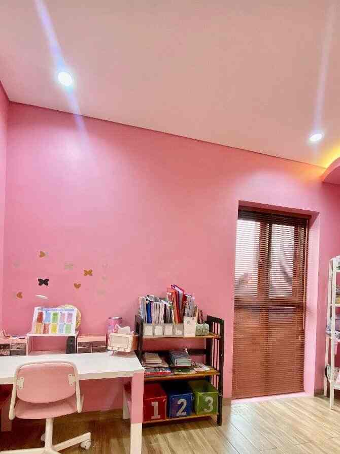 A pink-walled kids' room with wood-tone blinds, featuring a desk and colorful storage bins in a cozy atmosphere