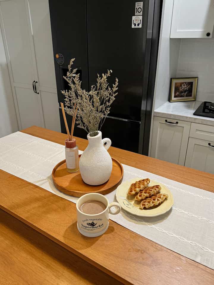 Warm brown wood tone kitchen featuring a Nordic style dining table with a vase and diffuser, creating a cozy home cafe atmosphere