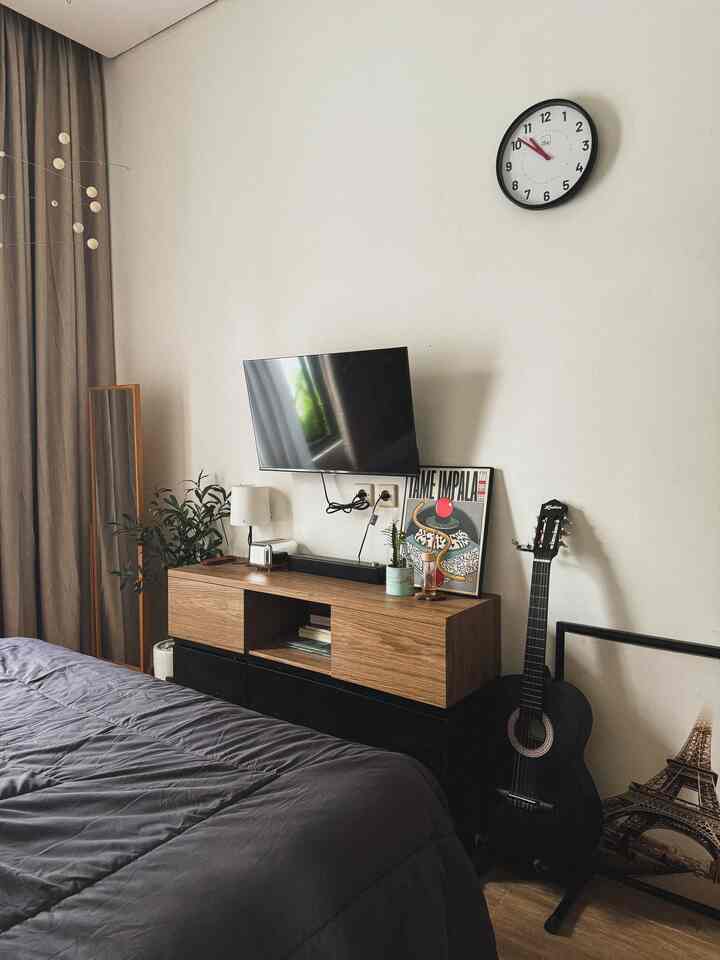 Gray-toned bedroom featuring wooden TV stand, wall clock, and a hanging mobile with a simple natural ambiance