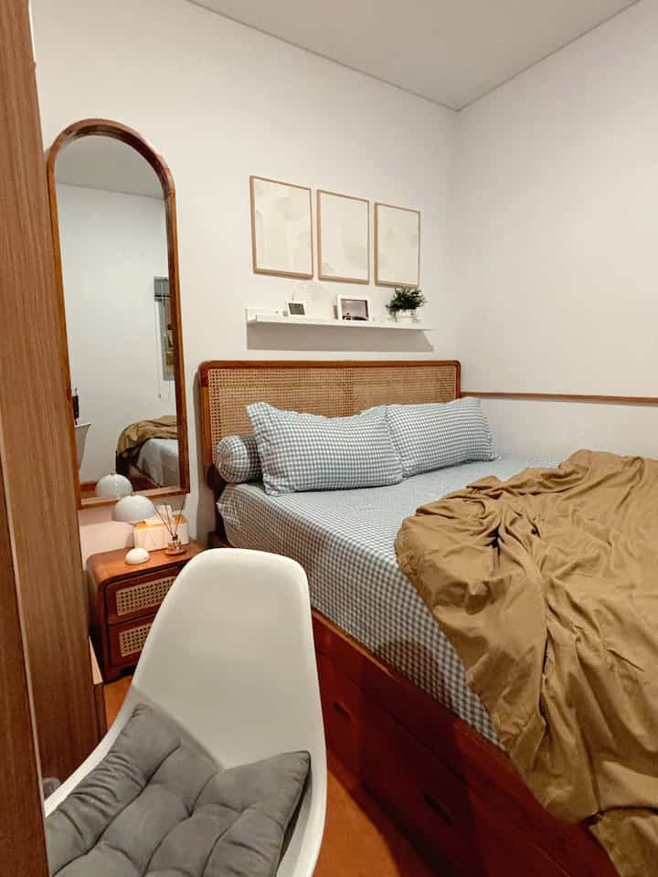 Cozy bedroom with natural wood tones featuring custom storage furniture and a full-length mirror in a compact space