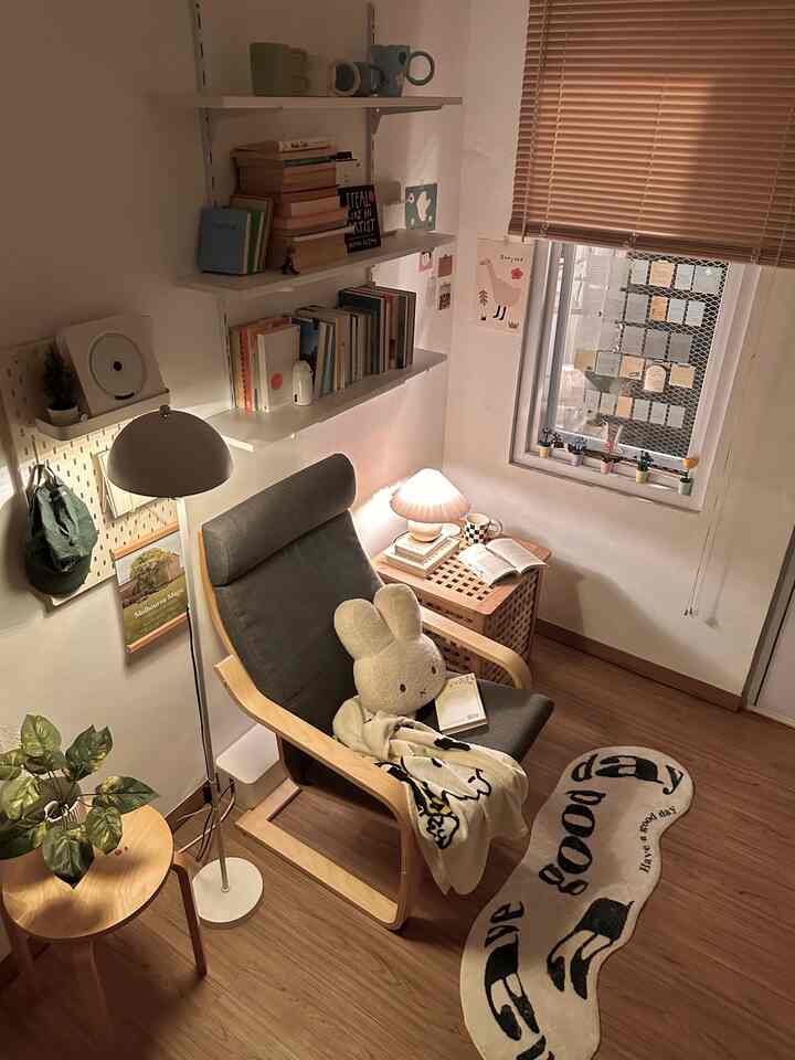 Light brown wood-tone floor and white walls define a minimal single-person reading space featuring bookshelf and armchair with cozy atmosphere