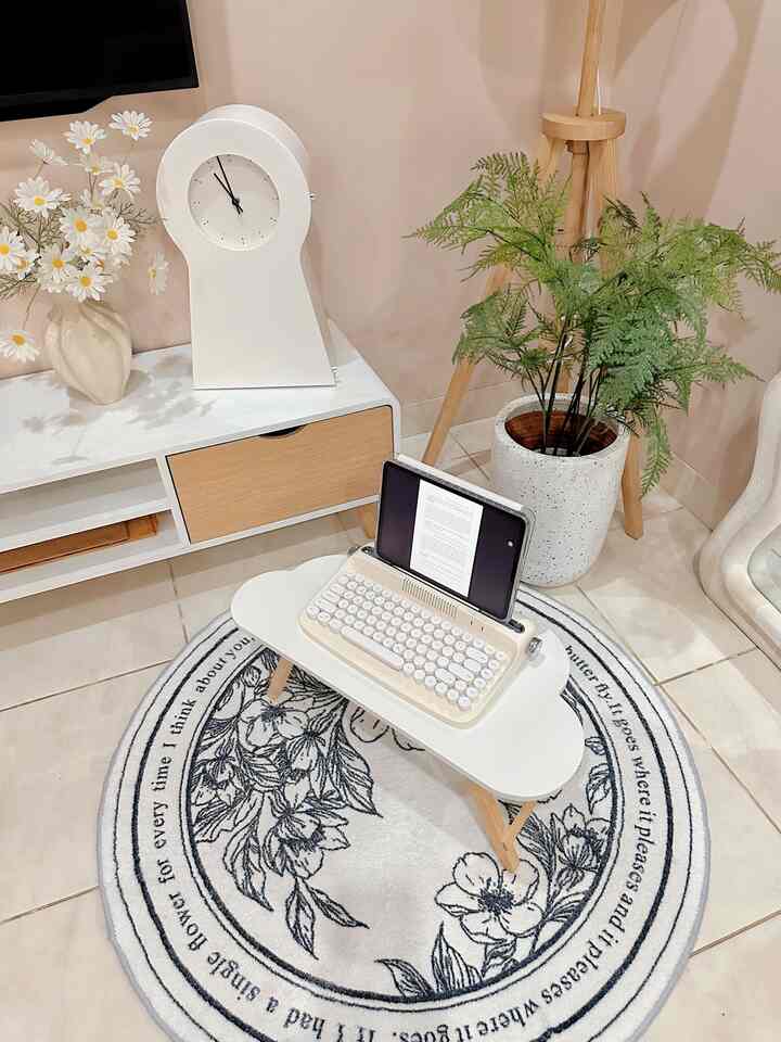 A white and natural toned small room featuring a small table, plant with pot, clock, creating a cozy workspace atmosphere