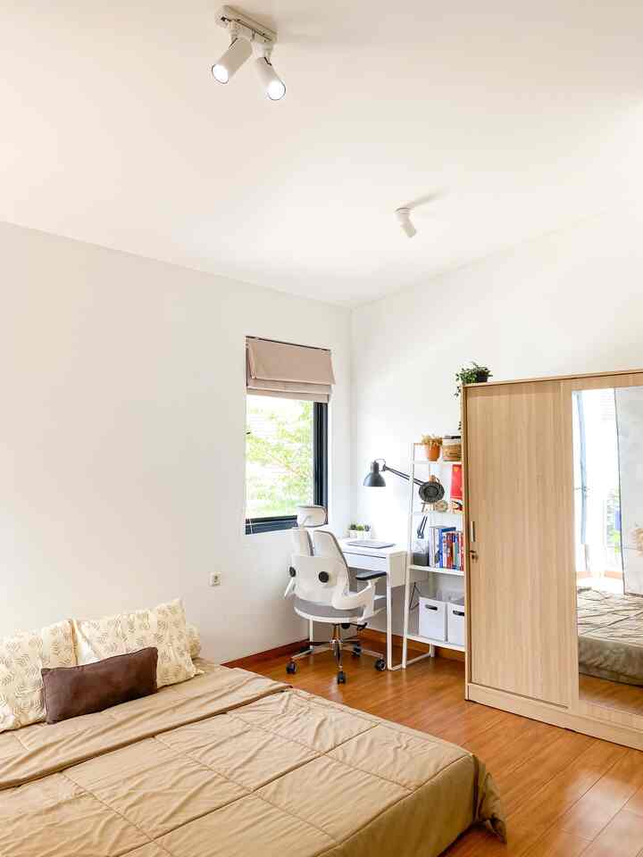 White and brown toned bedroom and workspace featuring a window-side desk and natural wood flooring, creating a serene atmosphere
