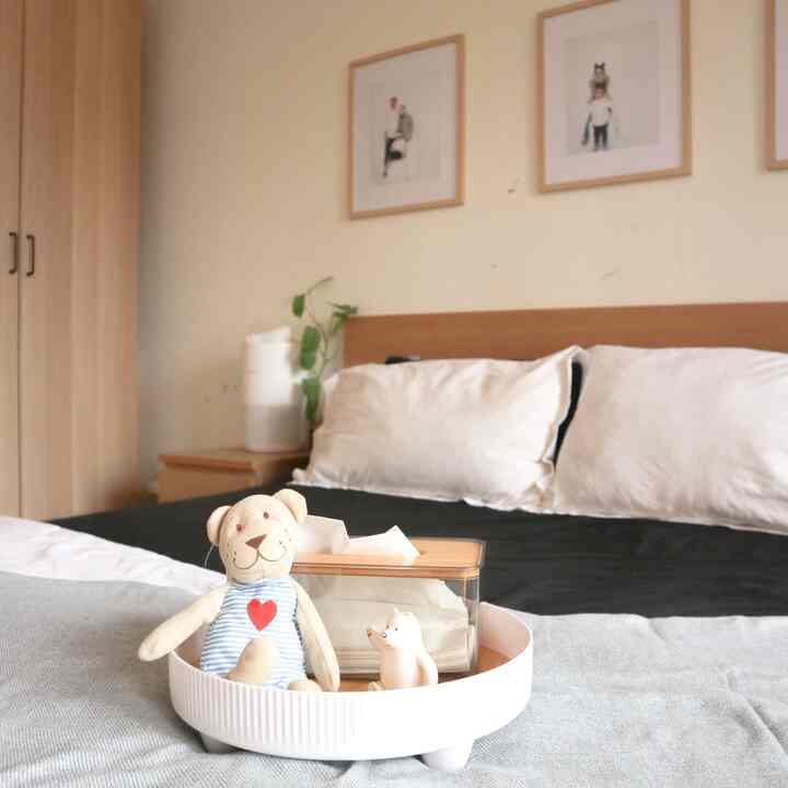 Beige-toned bedroom featuring bed with white and black bedding and a round tray holding a teddy bear, creating a cozy atmosphere