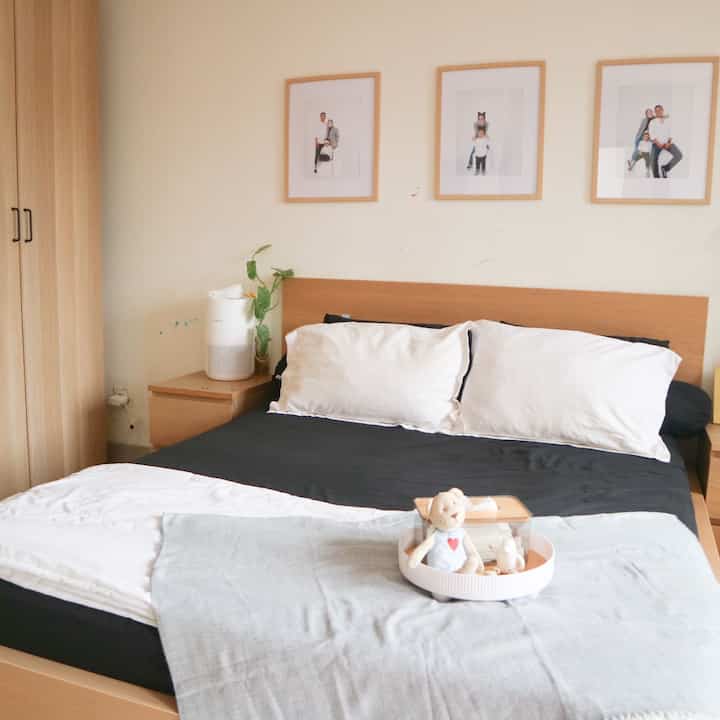 Bedroom with wood-tone furniture and white and black bedding, picture frames hung on wall creating a cozy atmosphere