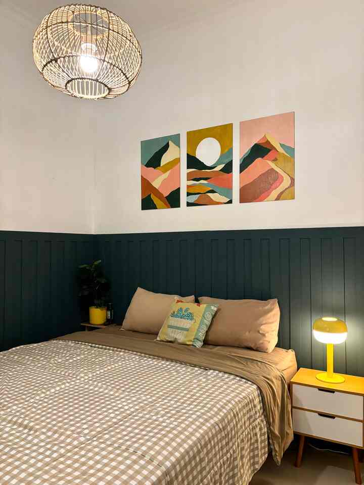 Bedroom with navy lower wall paneling and beige bedding, featuring wooden nightstand and yellow table lamp for cozy atmosphere