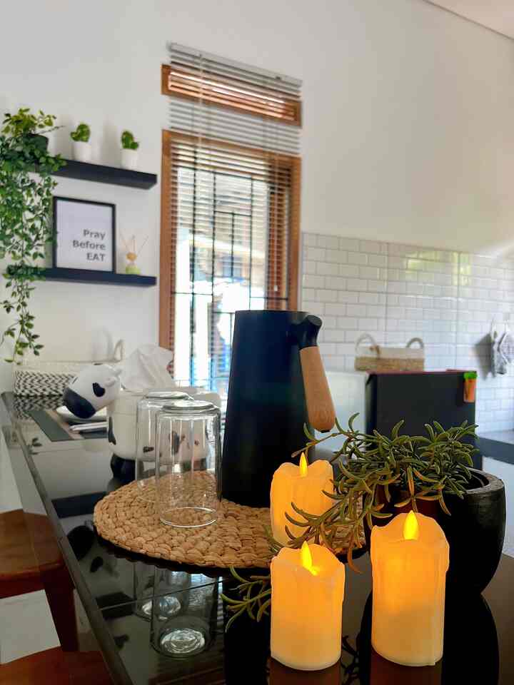 Modern natural kitchen space with white walls and tiles, black table featuring natural placemat, LED candles, and plants