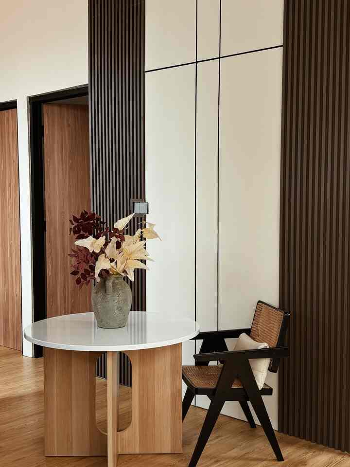 Natural wood tone and white-toned entrance area featuring a rattan armchair and round dining table with aesthetic design