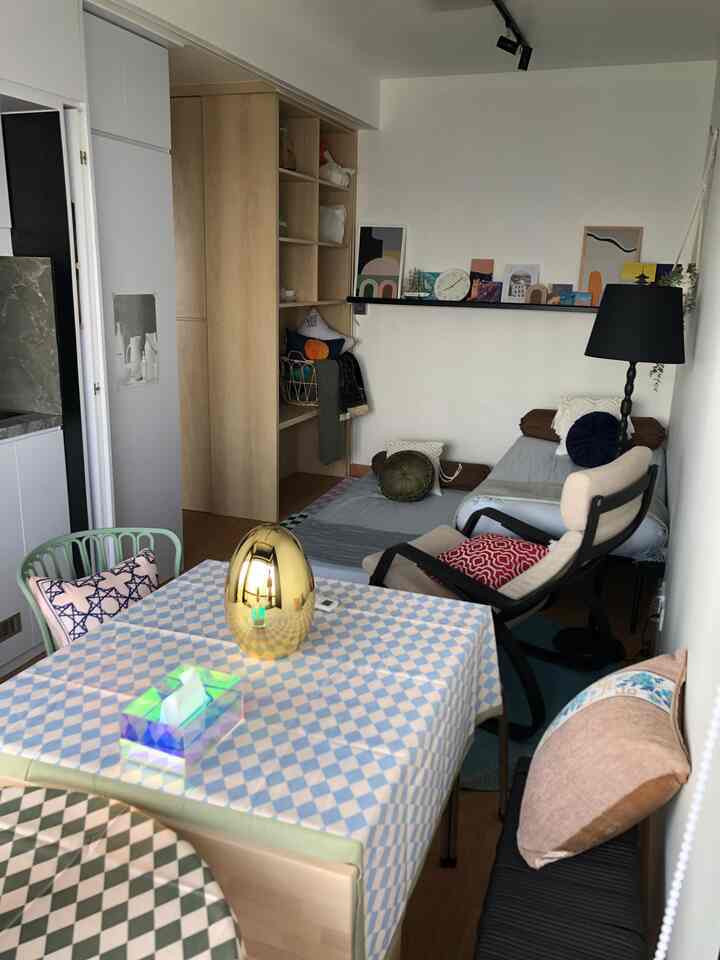 White walls and wood-tone shelving in a two-person dining room featuring a checkered tablecloth and cozy sofa bed setup