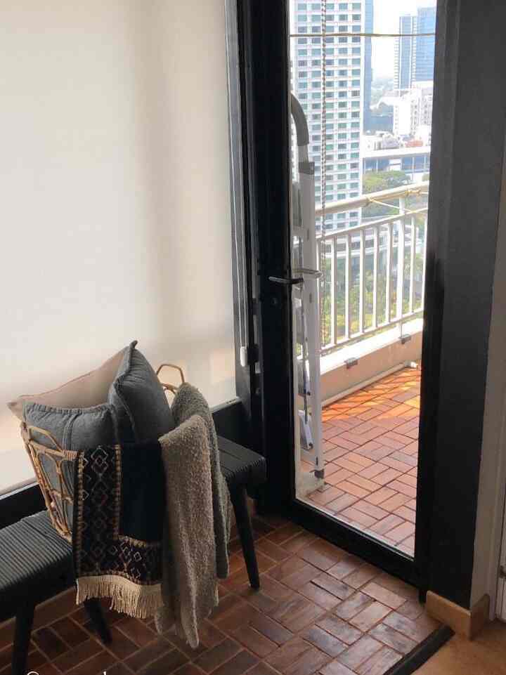Natural wood tone flooring in a long narrow space with a balcony visible, featuring cushions and storage basket creating a cozy atmosphere