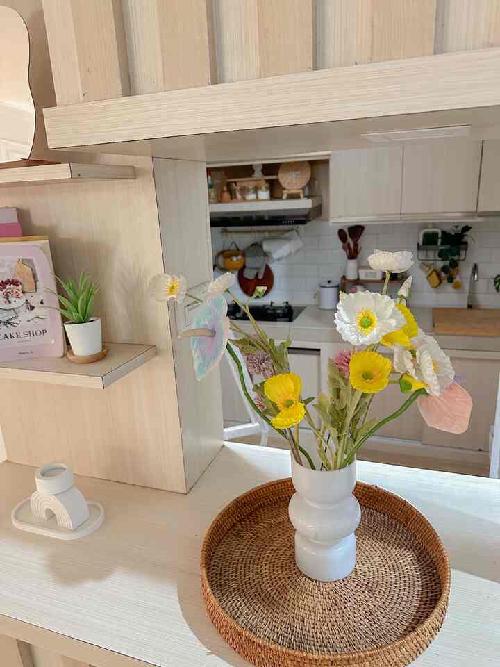 Beige and white toned kitchen space featuring a white vase with yellow and white flowers placed on a rattan tray, cozy interior