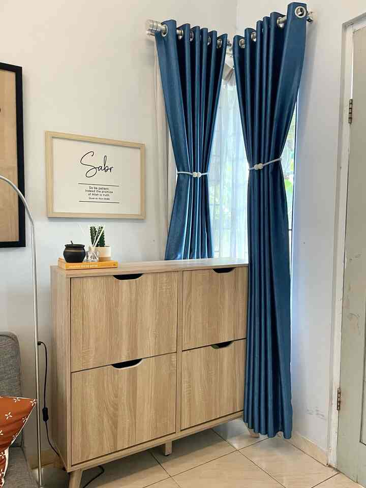 Ini adalah sudut entryway yang aku tata dengan tujuan menciptakan kesan pertama yang rapi sekaligus fungsional. Kabinet kayu dengan empat kompartemen ini sangat membantu menyimpan sepatu dan sandal, sehingga area ini tetap terorganisir. Desainnya yang sederhana dan bersih juga sejalan dengan konsep industrial minimalis yang aku terapkan di rumah.

Di atas kabinet, aku tambahkan beberapa elemen dekoratif seperti buku dan tanaman kecil untuk memberikan sentuhan personal tanpa menghilangkan kesan minimalis. Hiasan di dinding yang bertuliskan ‘Sabr’ menjadi pengingat yang tepat, memberikan nuansa tenang setiap kali aku atau tamu melewati area ini.

Tirai biru yang dipasang di jendela juga menambahkan aksen warna yang seimbang dengan elemen kayu. Selain berfungsi untuk menjaga privasi, warnanya membuat suasana ruangan terasa lebih segar.

Secara keseluruhan, area ini bukan hanya tempat penyimpanan, tetapi juga diharapkan bisa menyambut tamu dengan suasana yang rapi, nyaman, dan tetap estetis.

#Entryway #KabinetSepatu #EntranceDecorIdeas
#PintuMasuk #LivingRoomEntryWay #IndustrialMinimalist #WarnaCatRumah