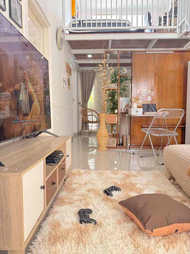 Beige and natural-tone living room, compact loft-style space featuring carpet with game controllers and transparent chair