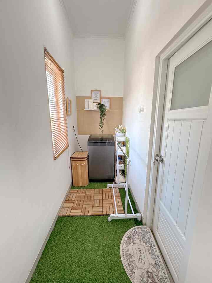 White and wood-tone long narrow laundry room featuring washing machine, storage rack, and drying stand in a tidy setup