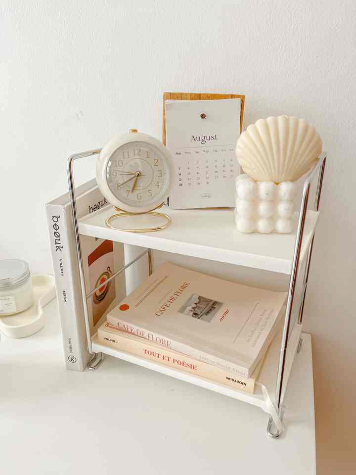 White-tone storage rack with clock, books, and shell-shaped decor on a simple desk surface
