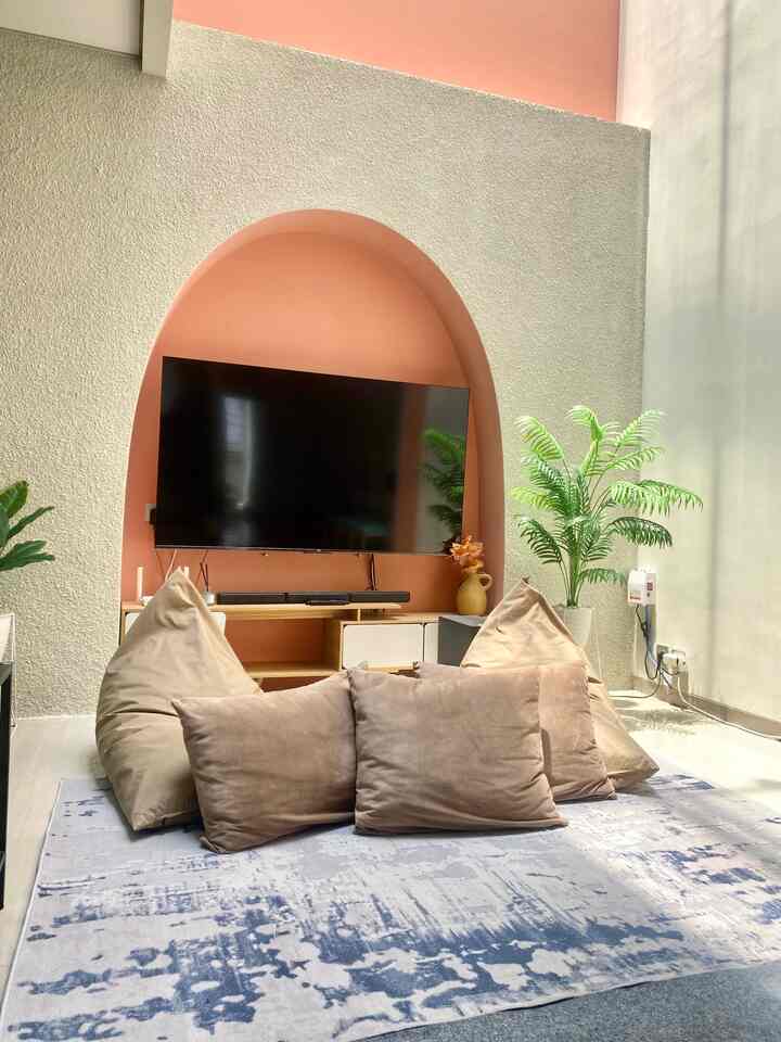 Living room with beige cushions on a blue patterned carpet, orange arch wall and green plant create a cozy atmosphere