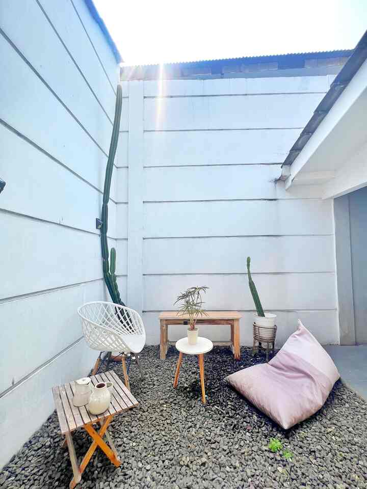 Outdoor yard with white walls and natural wooden furniture, featuring a pink bean bag and plants creating a cozy atmosphere