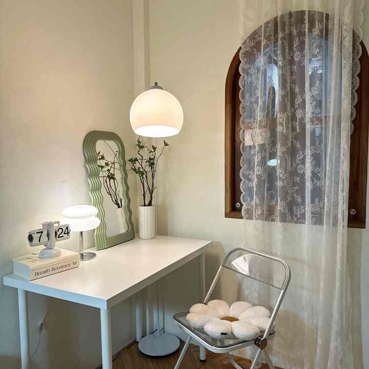 A compact home office with white and natural tones, featuring a simple desk, lace curtains, and soft lighting creating a cozy atmosphere