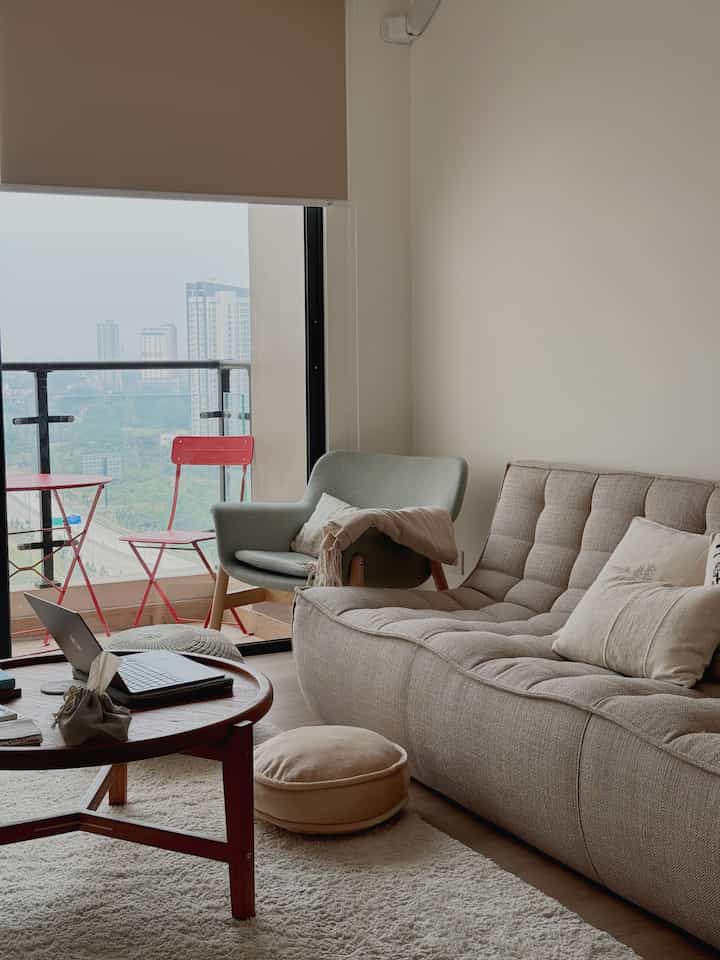Beige and natural toned living room featuring a beige sofa, gray armchair, round coffee table, and floor cushion, creating a cozy atmosphere